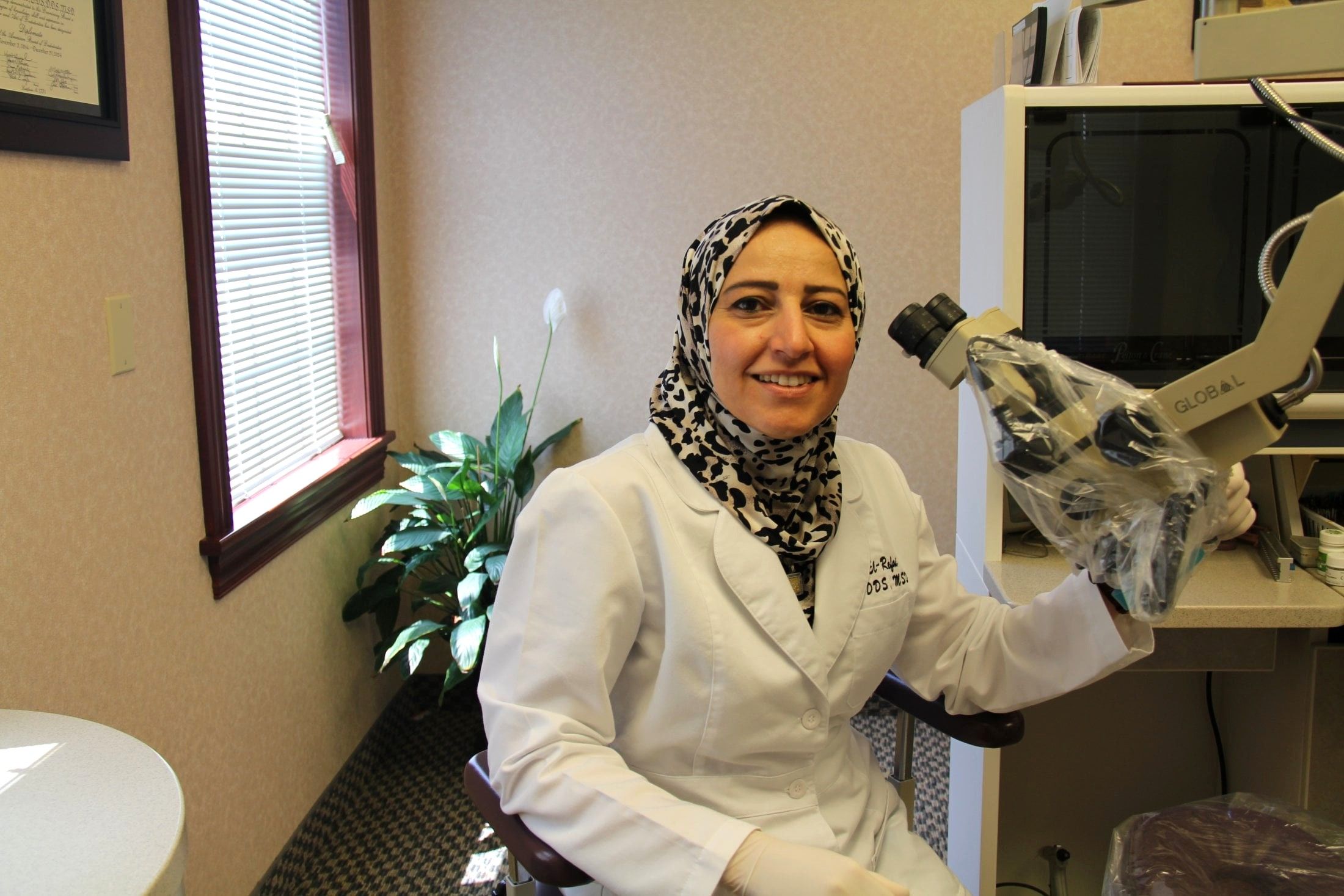 Dr. Nivine El-Refai smiling beside the surgical microscope in her Medina treatment room